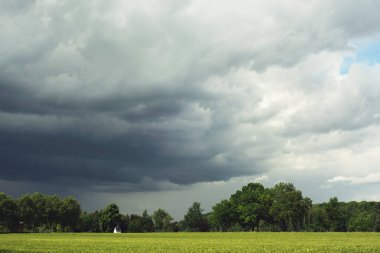 Yazın bulutlu bir gökyüzünün altında tarım arazileri ve ağaçlar.