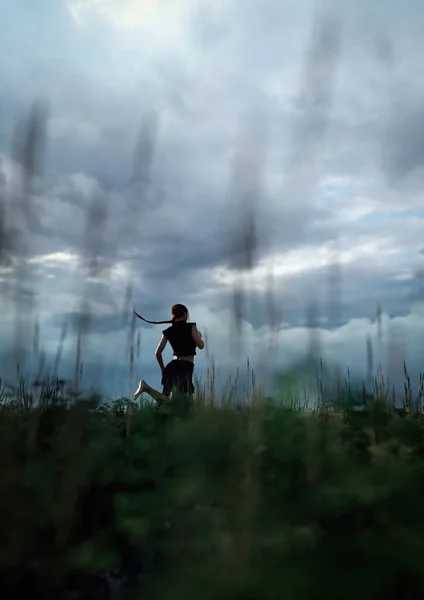 黒いスカートとシャツを着たポニーテールの女性は 暗い曇り空の下で背の高い草を持つフィールドを裸足で走ります 3Dレンダリング — ストック写真