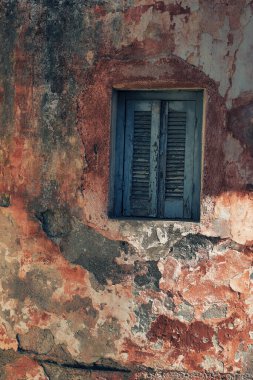 Kapalı mavi ahşap panjurlu küçük pencereli eskimiş pembe alçı duvar..