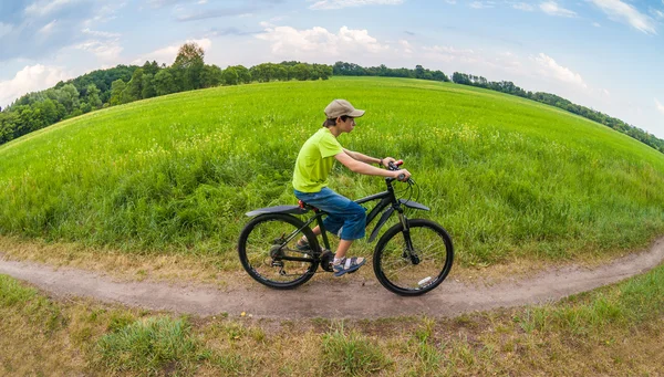 Landschaft durch Fischaugenobjektiv: Junge rast mit Fahrrad durch grünen Park — Stockfoto