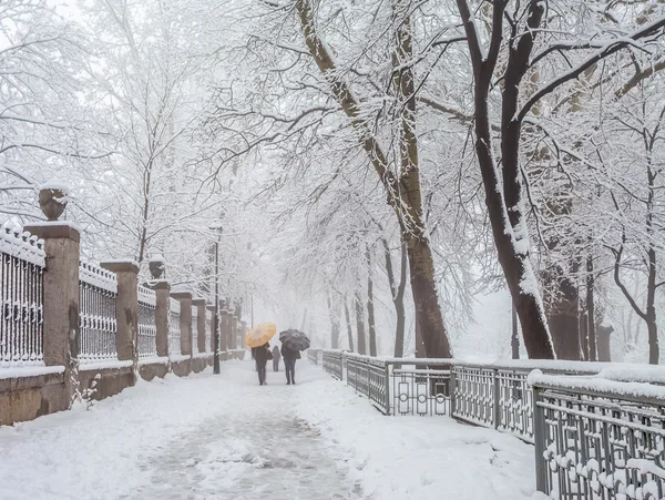 Снежный городской парк и люди с зонтиками — стоковое фото