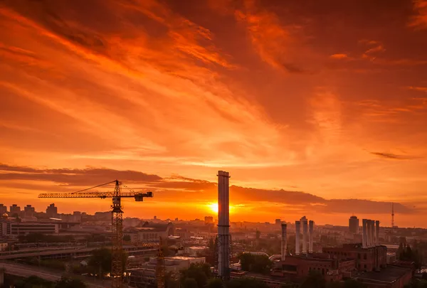 Gru nel cantiere sotto il tramonto e la silhouette della città — Foto Stock