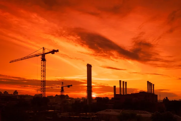 Gru nel cantiere sotto il tramonto e la silhouette della città — Foto Stock