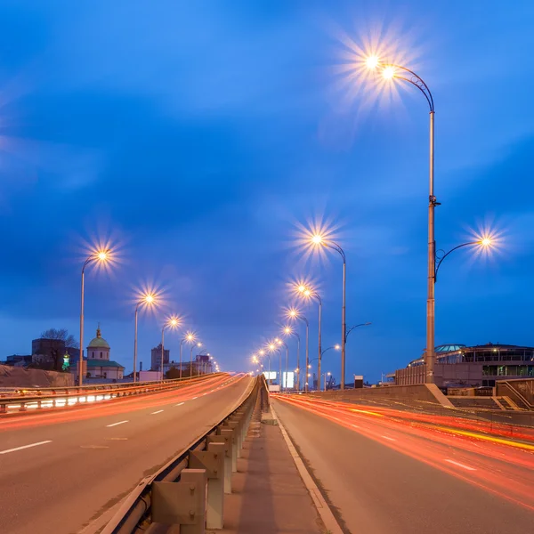 Voitures passent sur une route de ville le soir — Photo