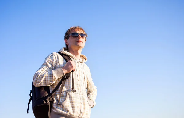 Happy man hiker holding backpack on a sunny day against a blue sky — Stock Photo, Image