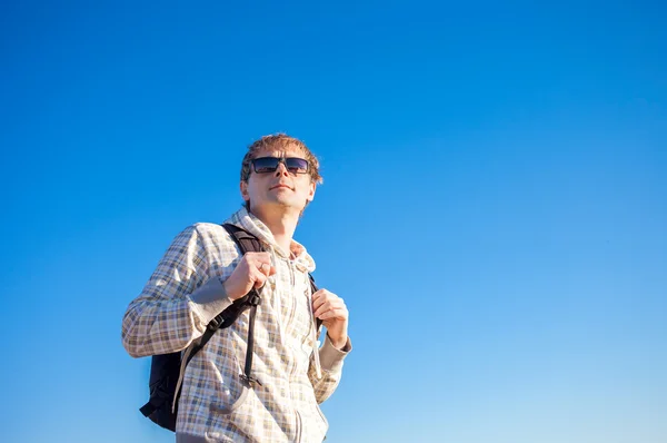 Happy man hiker holding backpack on a sunny day against a blue sky — Stock Photo, Image