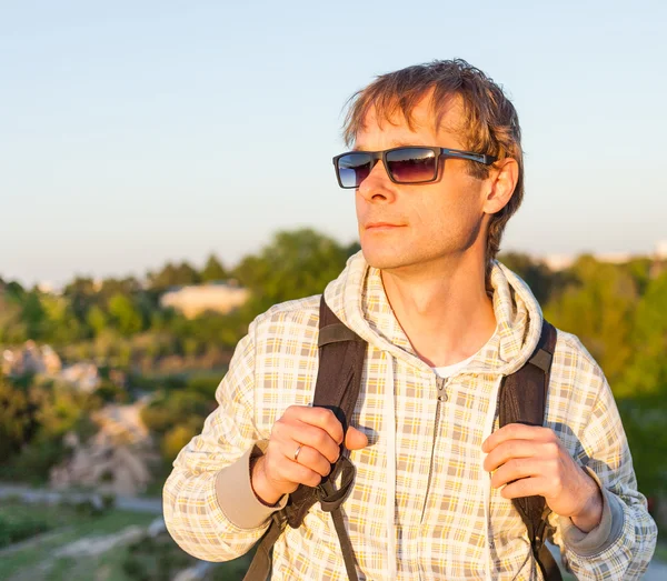 Happy man hiker holding backpack and looking at the sunset — Stock Photo, Image