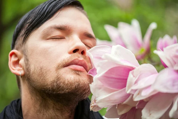 Portrait of young beautiful fashionable man in the flowered garden — Stock Photo, Image