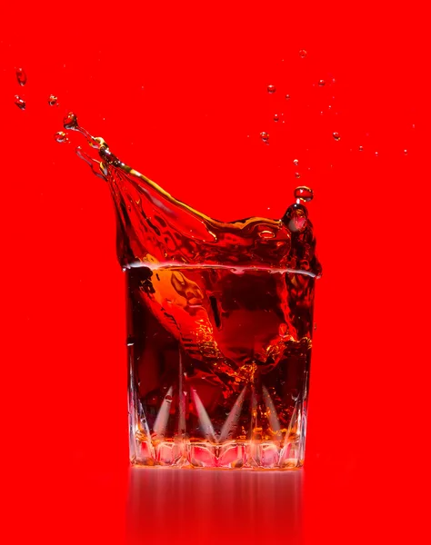 Vidrio con salpicadura de whisky sobre fondo rojo — Foto de Stock