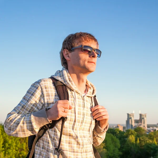 Hombre feliz excursionista sosteniendo la mochila y mirando el atardecer — Foto de Stock