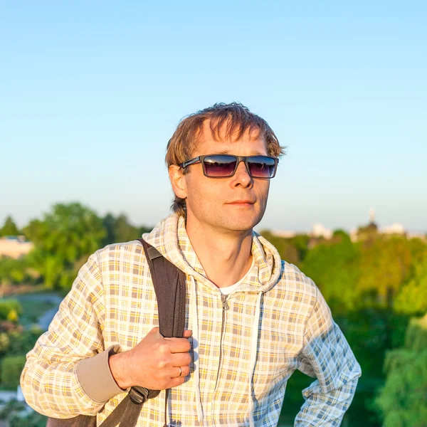Hombre feliz excursionista sosteniendo la mochila y mirando el atardecer — Foto de Stock