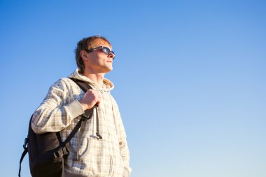 mutlu bir adam hiker karşı mavi gökyüzü güneşli bir sırt çantası elinde