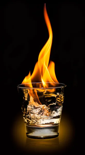 Vidrio con salpicadura de whisky y fuego sobre fondo negro — Foto de Stock