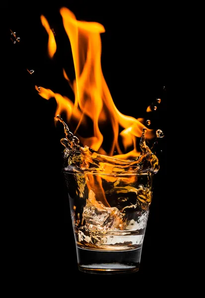 Bicchiere con spruzzi di whisky e fuoco su sfondo nero — Foto Stock
