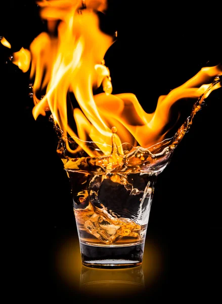 Vidrio con salpicadura de whisky y fuego sobre fondo negro — Foto de Stock