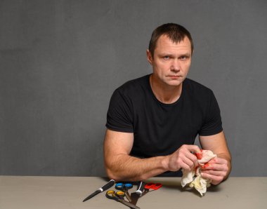 Kameraya bakan bir adamın fotoğrafı. Masada otururken elini makasla yaralıyor.