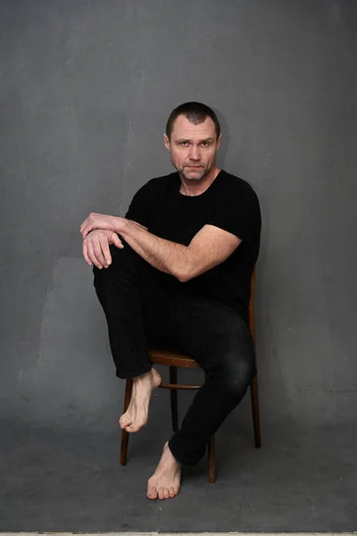 Serious adult male man on gray background looking directly at camera while sitting on chair — Stockfoto