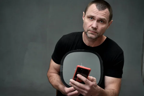 Hombre sosteniendo un teléfono inteligente en sus manos y mirando directamente a la cámara sobre un fondo gris — Foto de Stock