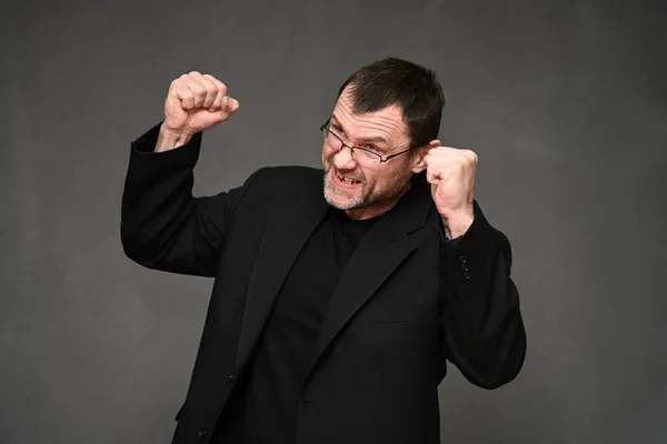 Caucásico hombre en una chaqueta con la ira con los puños en un fondo gris — Foto de Stock