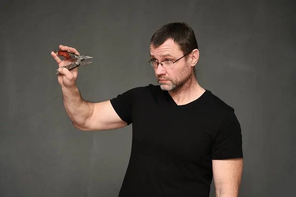 Man van middelbare leeftijd in een zwart T-shirt en bril met tang in zijn handen — Stockfoto