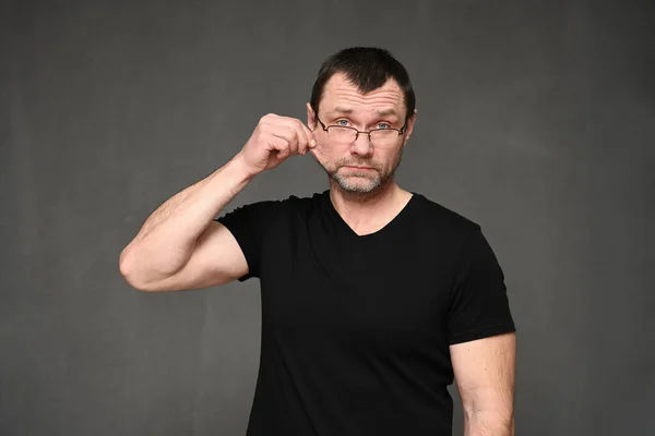 Portret van een volwassen man in een zwart t-shirt met bril toont creatief — Stockfoto