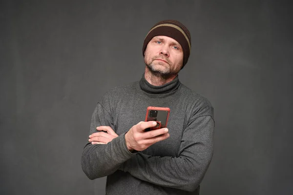 Un hombre con un teléfono mira a la cámara. Retrato sobre fondo gris en el estudio Fotos de stock libres de derechos