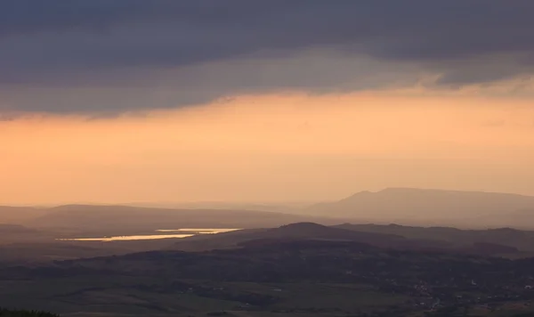Schwere Gewitterwolken sammeln sich bei Sonnenuntergang über dem Hügel in der Nähe eines Sees — Stockfoto