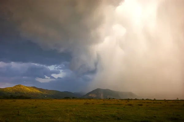 Nubes tormentosas que se aproximan sobre un prado cerca de montañas —  Fotos de Stock