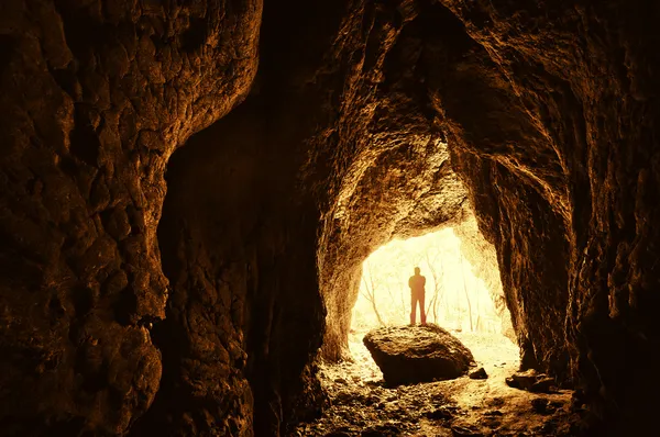 Cueva con el hombre de pie sobre una roca en frente de la entrada con árboles detrás de él —  Fotos de Stock