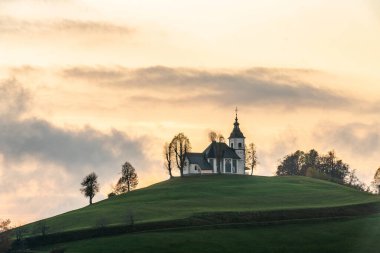 Bulutlu havada renkli bir gün batımı. Kilisenin manzarası Sv Sobota. Slovenya sonbaharda