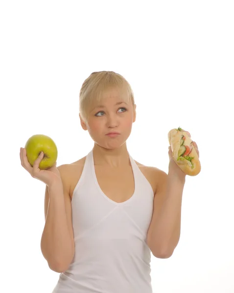 Тонкая женщина выбирает между яблоком и гамбургером Лицензионные Стоковые Изображения