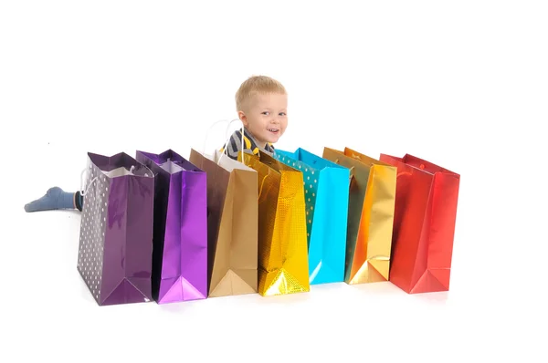 Schattige jongen met shopping tassen na het winkelen. geïsoleerd op wit — Stockfoto