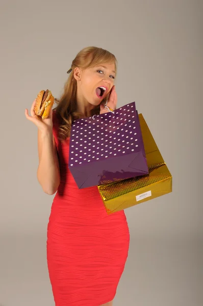 Mujer hermosa joven con algunas bolsas de compras y hamburguesa aislada en blanco — Foto de Stock