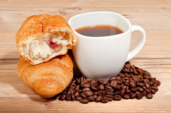 Croissant with coffee and beans on wooden background — Stock Photo, Image
