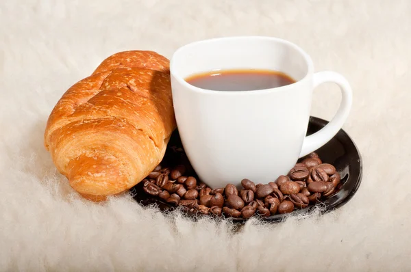 Croissant met koffie en bonen op bont achtergrond — Stockfoto