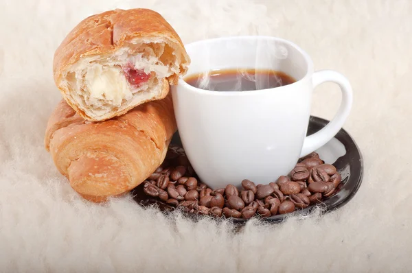 Croissant met koffie en bonen op bont achtergrond — Stockfoto