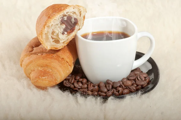 Croissant met koffie en bonen op bont achtergrond — Stockfoto