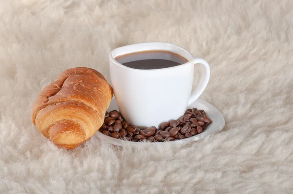 Croissant met koffie en bonen op bont achtergrond — Stockfoto