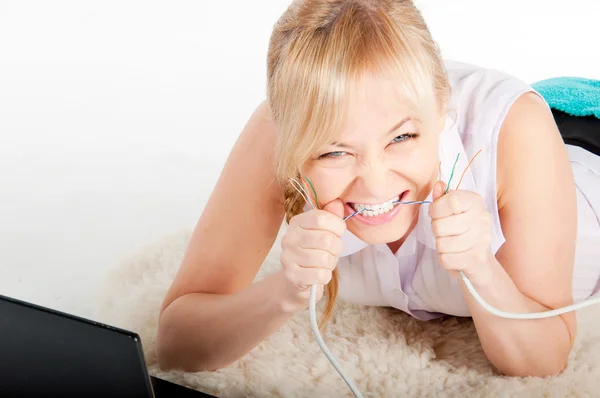 Hermosa joven con una computadora portátil que muerde el cable de la red en cuadros calientes — Foto de Stock