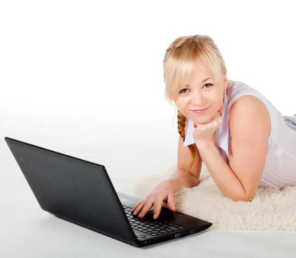 Beautiful young woman with a laptop lies on warm plaid — Stock Photo, Image