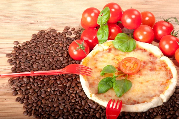 Close-up van pizza met koffiebonen, twee rode vorken, tomaten, kaas en basilicum op houten achtergrond — Stockfoto