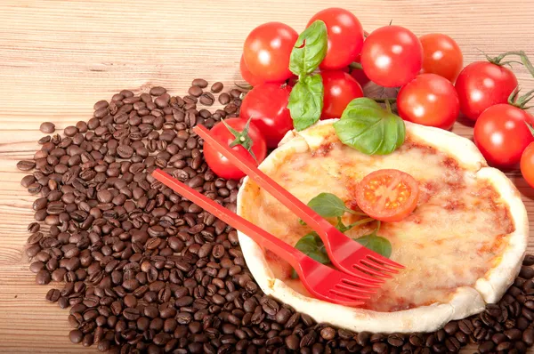 Close-up van pizza met koffiebonen, twee rode vorken, tomaten, kaas en basilicum op houten achtergrond — Stockfoto