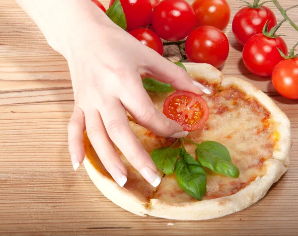 Close-up van pizza met tomaten, kaas, basi en vrouw handsl op houten achtergrond — Stockfoto