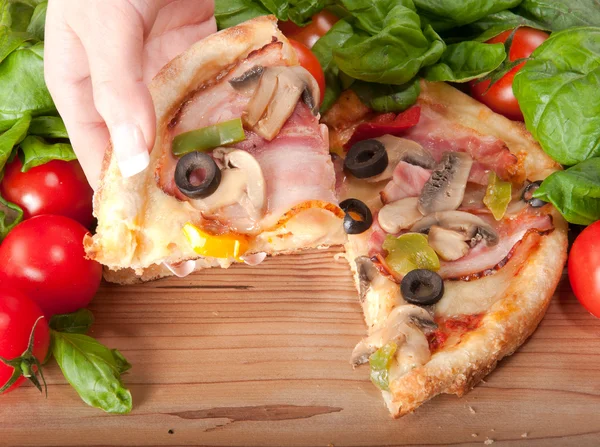 Close-up van pizza met tomaten, kaas, basi en vrouw handsl op houten achtergrond — Stockfoto