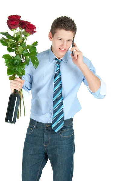 Young business man in blue shirt and tie with bottle of wine, bunch of red roses speaking on a phone — Stock Photo, Image