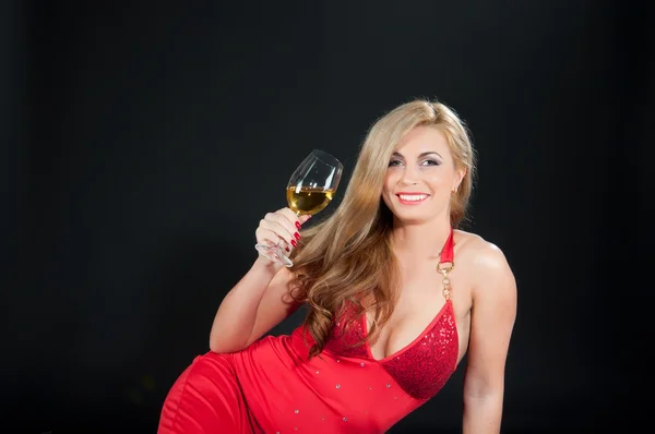 Sexy blondýnka v červených šatech s sklenku vína tmavém pozadí — Stock fotografie