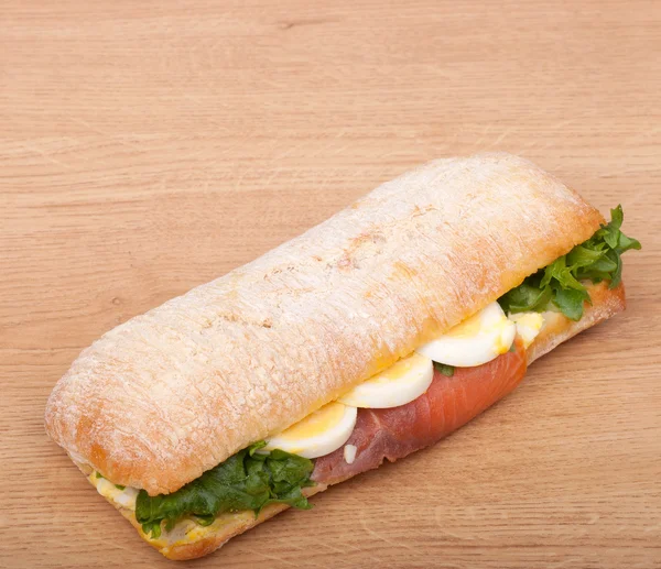 Real sandwich with smoked salmon, eggs and green on a wooden background — Stock Photo, Image