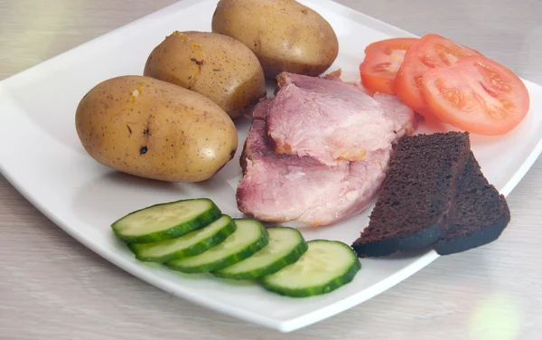 Carne di maiale alla griglia con patate in bolo, verdure e pane. con effetto lente — Foto Stock