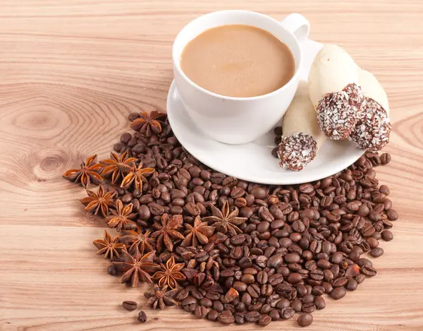 Coffee cup, anise on coffee beans, sweets on the wooden background — Stock Photo, Image