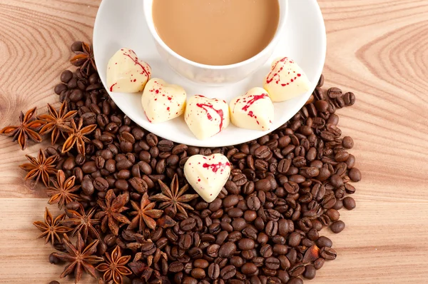 Чашка кофе с бобами и конфеты с белым шоколадом на деревянном фоне — стоковое фото